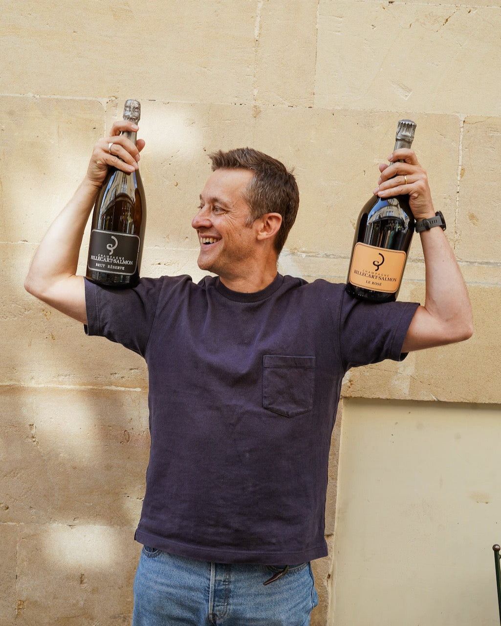 Man holding two bottles of champagne against a beige wall